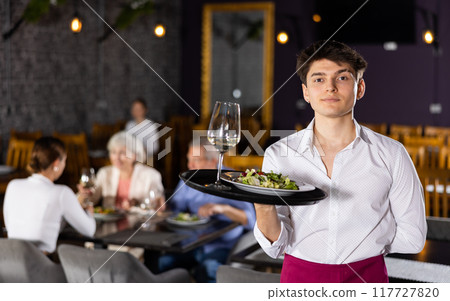 Young male waiter posing with tray in restaurant 117727820