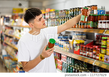 man chooses tomato sauce in supermarket. 117727829