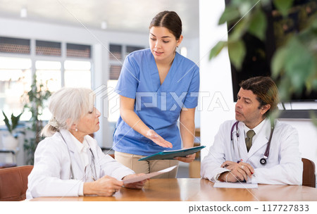 Young female physician discussing diagnosis of patients with colleagues 117727833