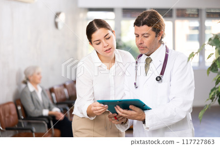 Adult male doctor and young woman with folder of documents Adult male doctor and young woman with folder of documents 117727863