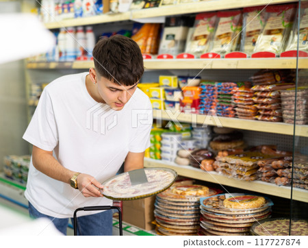Young male customer diligently picking out frozen pizza Young male customer diligently picking out frozen pizza 117727874