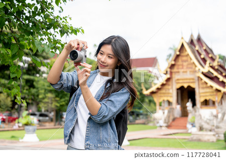 A happy, charming Asian female tourist is enjoying taking a photo and strolling in a Thai temple. A happy, charming Asian female tourist is enjoying taking a photo and strolling in a Thai temple. 117728041