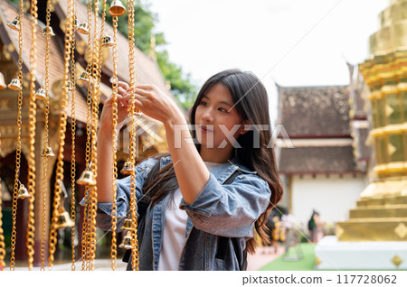 A positive Asian female tourist is hanging a bell for luck in a temple during her visit to Thailand. A positive Asian female tourist is hanging a bell for luck in a temple during her visit to Thailand. 117728062