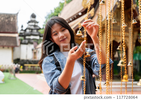 A positive Asian female tourist is hanging a bell for luck in a temple during her visit to Thailand. A positive Asian female tourist is hanging a bell for luck in a temple during her visit to Thailand. 117728064