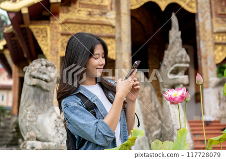 A positive Asian female tourist is using her smartphone while visiting a temple in Thailand. A positive Asian female tourist is using her smartphone while visiting a temple in Thailand. 117728079