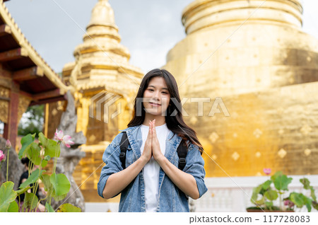 An attractive Asian female tourist is putting her hands together in a prayer position in a temple. 117728083
