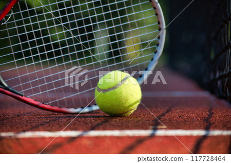 Close-up of tennis ball and racket against net on clay court Close-up of tennis ball and racket against net on clay court 117728464