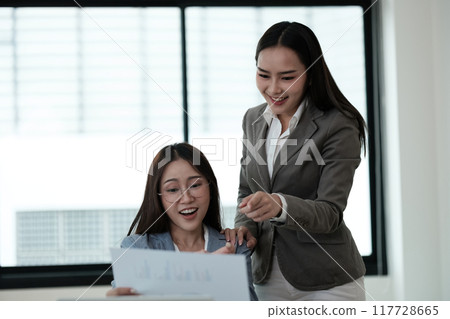 Two women are sitting at a table looking at a piece of paper Two women are sitting at a table looking at a piece of paper 117728665