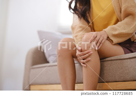 A woman sits on a couch with her knee propped up 117728685