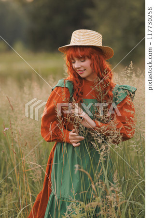 A shepherdess woman with red hair and a green dress sits in a field of flowers. A shepherdess woman with red hair and a green dress sits in a field of flowers. 117730258