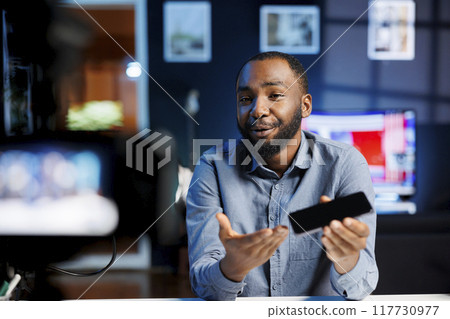 African american internet star being sponsored by partnering brand to do smartphone unboxing content. Tech expert does influencer marketing, doing product placement of mobile phone African american internet star being sponsored by partnering brand to do smartphone unboxing content. Tech expert does influencer marketing, doing product placement of mobile phone 117730977