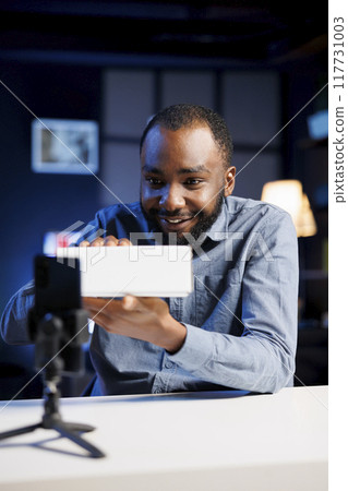 Content creator filming technology review of newly launched digital device, excited to unbox it and present specifications to audience. Online star laughing while showing product to fans 117731003