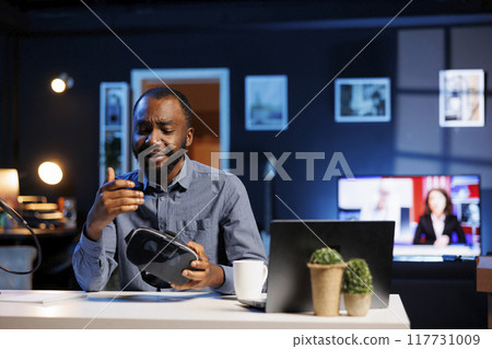 Tech influencer filming sponsored branded content, unboxing newly released VR glasses product. Cheerful entertainer presenting virtual reality headset parameters to subscribers Tech influencer filming sponsored branded content, unboxing newly released VR glasses product. Cheerful entertainer presenting virtual reality headset parameters to subscribers 117731009