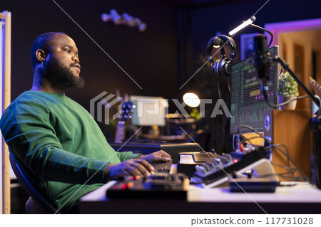 Sound engineer playing piano and mixing tunes on digital software, composing new songs and adding audio effects in post production. Artist composer creating soundtracks for music industry. 117731028