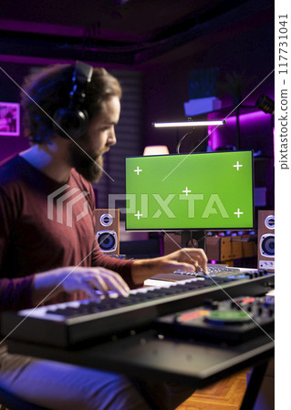 Musician learning to play electronic keyboard synthesizer in home studio, watching tutorial online via greenscreen on computer. Music composer playing midi controller notes, rehearsal practice. Musician learning to play electronic keyboard synthesizer in home studio, watching tutorial online via greenscreen on computer. Music composer playing midi controller notes, rehearsal practice. 117731041