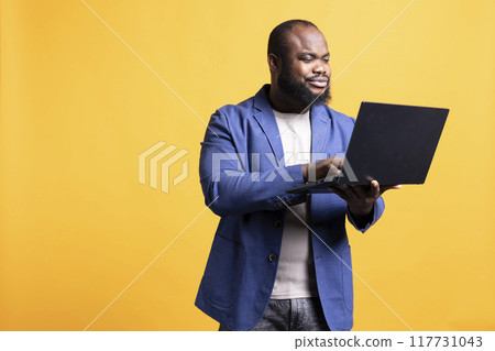 Smiling african american man looking at business diagram and figures on laptop, isolated over studio background. Upbeat worker checking company financial annual report charts on notebook Smiling african american man looking at business diagram and figures on laptop, isolated over studio background. Upbeat worker checking company financial annual report charts on notebook 117731043