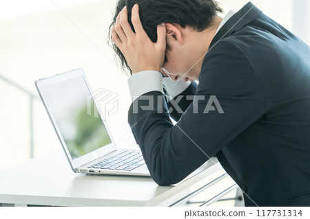 A young male businessman holding his head at his desk A young male businessman holding his head at his desk 117731314