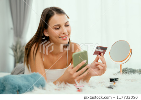 Young woman lying on bed using online payment app. Unveiling Young woman lying on bed using online payment app. Unveiling 117732050