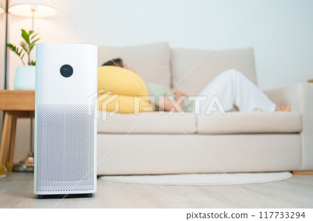 Air Purifier with woman relax and sleep on sofa. Purification system for filter and cleaning dust PM2.5 HEPA and virus in home. Allergy, Pure air, health, Wellness lifestyle and Air Pollution 117733294