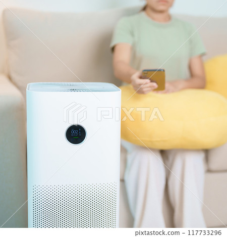 Woman turn on Air Purifier in living room by smartphone application. Purification system for filter and cleaning dust PM2.5 HEPA and virus. Allergy, Pure air, health lifestyle and Air Pollution 117733296