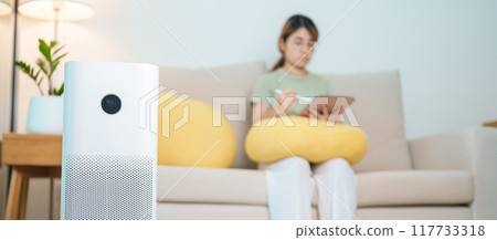 Air Purifier with woman relax and use tablet on sofa. Purification system for filter and cleaning dust PM2.5 HEPA and virus in home. Allergy, Pure air, health, Wellness lifestyle and Air Pollution 117733318