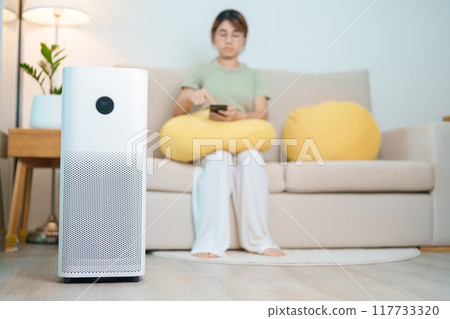 Air Purifier with woman relax and use smartphone on sofa. Purification system for filter and cleaning dust PM2.5 HEPA and virus in home. Allergy, Pure air, health, Wellness lifestyle and Air Pollution Air Purifier with woman relax and use smartphone on sofa. Purification system for filter and cleaning dust PM2.5 HEPA and virus in home. Allergy, Pure air, health, Wellness lifestyle and Air Pollution 117733320