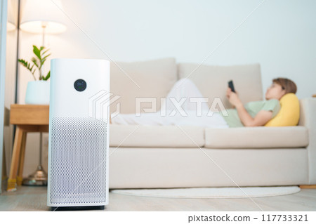 Air Purifier with woman relax and use smartphone on sofa. Purification system for filter and cleaning dust PM2.5 HEPA and virus in home. Allergy, Pure air, health, Wellness lifestyle and Air Pollution 117733321