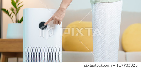 Woman turn on Air Purifier in living room. Purification system for filter and cleaning dust PM2.5 HEPA and virus in home. Allergy, Pure air, health lifestyle, Wellness life and Air Pollution 117733323