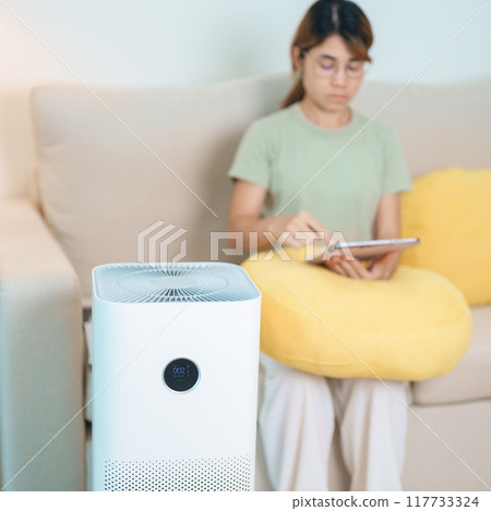 Air Purifier with woman relax and use tablet on sofa. Purification system for filter and cleaning dust PM2.5 HEPA and virus in home. Allergy, Pure air, health, Wellness lifestyle and Air Pollution 117733324