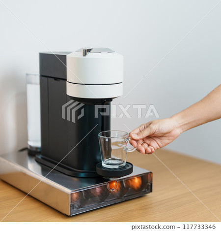 hand making Espresso Coffee by Coffee Maker Machine with Capsule of roasted coffee bean on wood table bar. Daily beverage drink at Home, Apartment and Office concept 117733346