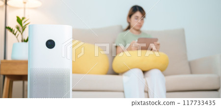Air Purifier with woman relax and use tablet on sofa. Purification system for filter and cleaning dust PM2.5 HEPA and virus in home. Allergy, Pure air, health, Wellness lifestyle and Air Pollution 117733435