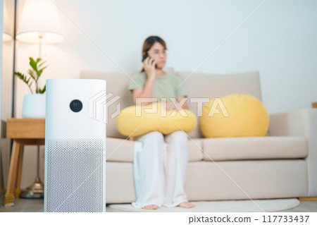 Air Purifier with woman relax and use smartphone on sofa. Purification system for filter and cleaning dust PM2.5 HEPA and virus in home. Allergy, Pure air, health, Wellness lifestyle and Air Pollution Air Purifier with woman relax and use smartphone on sofa. Purification system for filter and cleaning dust PM2.5 HEPA and virus in home. Allergy, Pure air, health, Wellness lifestyle and Air Pollution 117733437