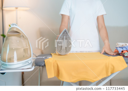Woman hold Electric hot iron press T shirt clothes on ironing board, Intelligent automatic steam iron. Laundry, Housework, Housekeeping, Domestic hygiene, household of chores and daily routine concept Woman hold Electric hot iron press T shirt clothes on ironing board, Intelligent automatic steam iron. Laundry, Housework, Housekeeping, Domestic hygiene, household of chores and daily routine concept 117733445