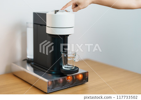 hand making Espresso Coffee by Coffee Maker Machine with Capsule of roasted coffee bean on wood table bar. Daily beverage drink at Home, Apartment and Office concept 117733502