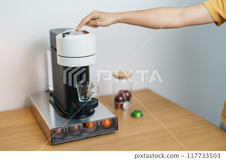 hand making Espresso Coffee by Coffee Maker Machine with Capsule of roasted coffee bean on wood table bar. Daily beverage drink at Home, Apartment and Office concept 117733503