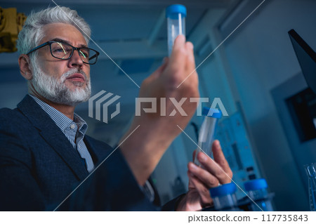 Scientist in the laboratory holding test tube and intently looking at its contents 117735843
