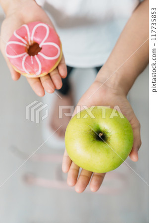 woman on weight scale and hand hold green Apple and donut, choose between fruit is Healthy and sweet is Unhealthy junk food. Dieting control, Weight loss, Obesity, eating lifestyle and nutrition woman on weight scale and hand hold green Apple and donut, choose between fruit is Healthy and sweet is Unhealthy junk food. Dieting control, Weight loss, Obesity, eating lifestyle and nutrition 117735853