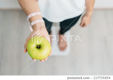 woman on weight scale and hand hold green Apple, choose fruit is Healthy food. Dieting control, Weight loss, Obesity, eating lifestyle and nutrition concepts woman on weight scale and hand hold green Apple, choose fruit is Healthy food. Dieting control, Weight loss, Obesity, eating lifestyle and nutrition concepts 117735854