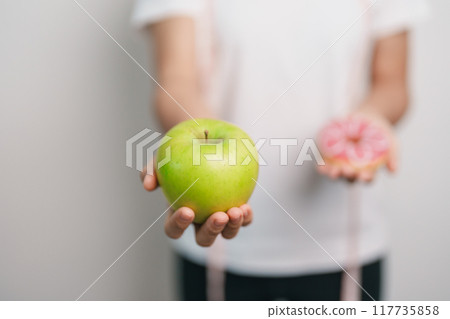 woman hand hold green Apple and donut, female fitness choose between fruit is Healthy and sweet is Unhealthy junk food. Dieting control, Weight loss, Obesity, eating lifestyle and nutrition concept woman hand hold green Apple and donut, female fitness choose between fruit is Healthy and sweet is Unhealthy junk food. Dieting control, Weight loss, Obesity, eating lifestyle and nutrition concept 117735858