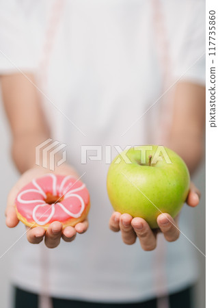 woman hand hold green Apple and donut, female fitness choose between fruit is Healthy and sweet is Unhealthy junk food. Dieting control, Weight loss, Obesity, eating lifestyle and nutrition concept woman hand hold green Apple and donut, female fitness choose between fruit is Healthy and sweet is Unhealthy junk food. Dieting control, Weight loss, Obesity, eating lifestyle and nutrition concept 117735860