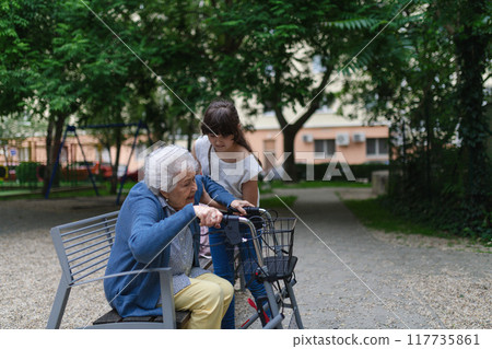 Girl helping gradma with walker to stand up from bench. 117735861