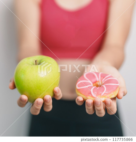 woman hand hold green Apple and donut, female fitness choose between fruit is Healthy and sweet is Unhealthy junk food. Dieting control, Weight loss, Obesity, eating lifestyle and nutrition concept 117735866