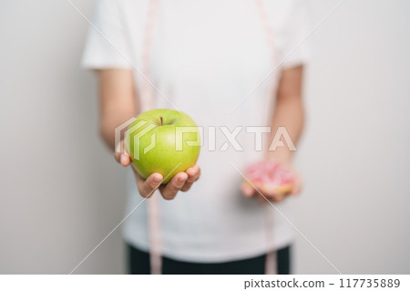 woman hand hold green Apple and donut, female fitness choose between fruit is Healthy and sweet is Unhealthy junk food. Dieting control, Weight loss, Obesity, eating lifestyle and nutrition concept woman hand hold green Apple and donut, female fitness choose between fruit is Healthy and sweet is Unhealthy junk food. Dieting control, Weight loss, Obesity, eating lifestyle and nutrition concept 117735889