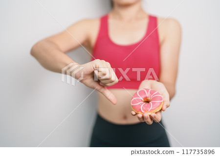 woman hand hold Donut with tape measure, choose stop eating sweet is Unhealthy ealthy food. Dieting control, Weight loss, Obesity, eating lifestyle and nutrition concepts woman hand hold Donut with tape measure, choose stop eating sweet is Unhealthy ealthy food. Dieting control, Weight loss, Obesity, eating lifestyle and nutrition concepts 117735896
