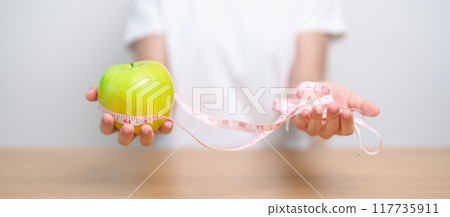 woman hand hold green Apple with tape measure, happy female choose fruit is Healthy food. Dieting control, Weight loss, Obesity, eating lifestyle and nutrition concepts woman hand hold green Apple with tape measure, happy female choose fruit is Healthy food. Dieting control, Weight loss, Obesity, eating lifestyle and nutrition concepts 117735911
