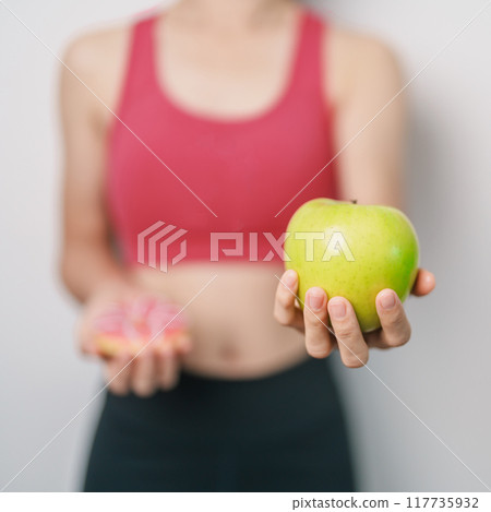 woman hand hold green Apple and donut, female fitness choose between fruit is Healthy and sweet is Unhealthy junk food. Dieting control, Weight loss, Obesity, eating lifestyle and nutrition concept 117735932