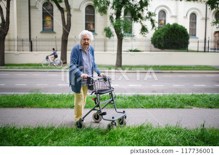 Beautiful elderly woman walking on city street with rollator, going shopping to the store. 117736001