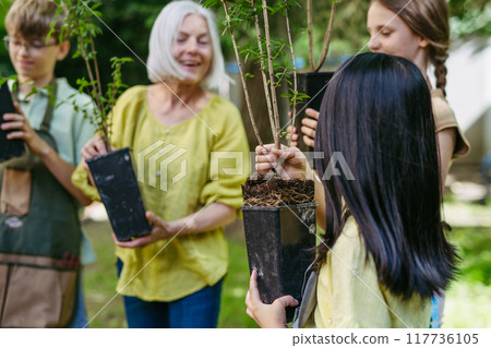 Kids learning about fruit tree seedling and fruit bushes, taking care of school garden during outdoor sustainable education, class in forest school. Concept of experiential learning and ecoliteracy. 117736105