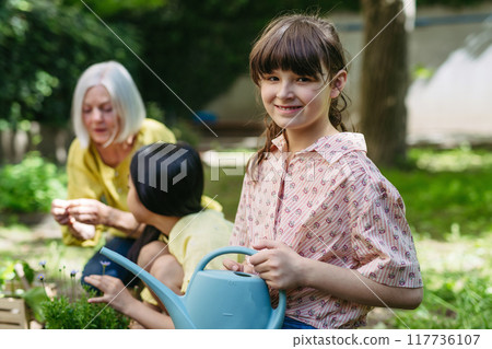 Portrait of cute schoolgirl taking care of plants in school garden during at outdoor sustainable education class. Concept of experiential learning and ecoliteracy. 117736107