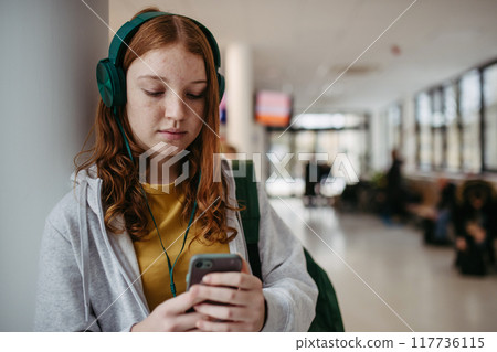 Teenage girl waiting in hospital corridor, listening music. Adolescent patient coming to hospital for examination. 117736115